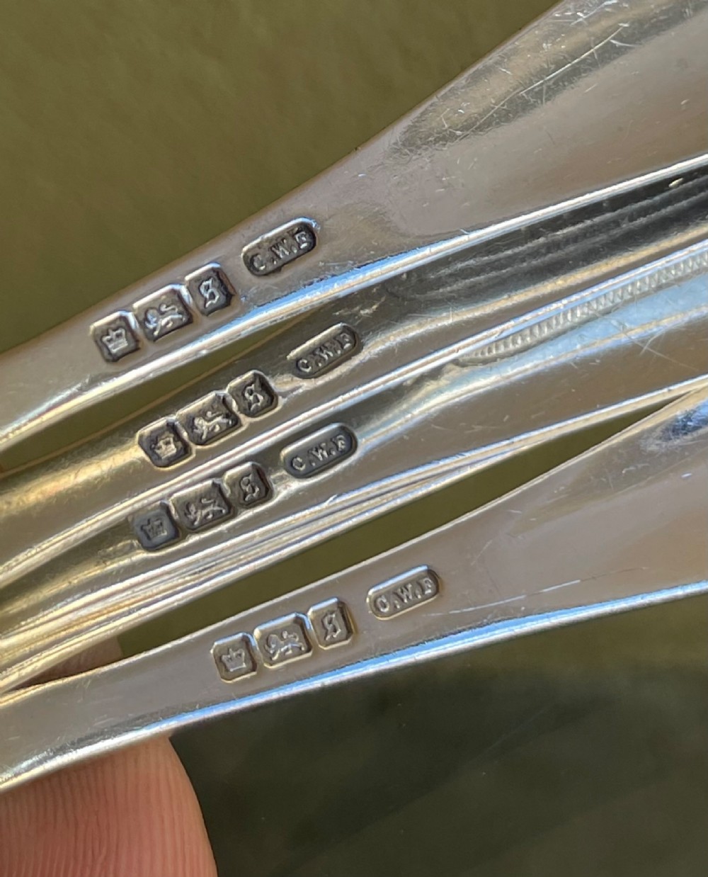 A set of five George V silver egg spoons featuring decorative engraved scrolled handles laid flat in a row. View IV