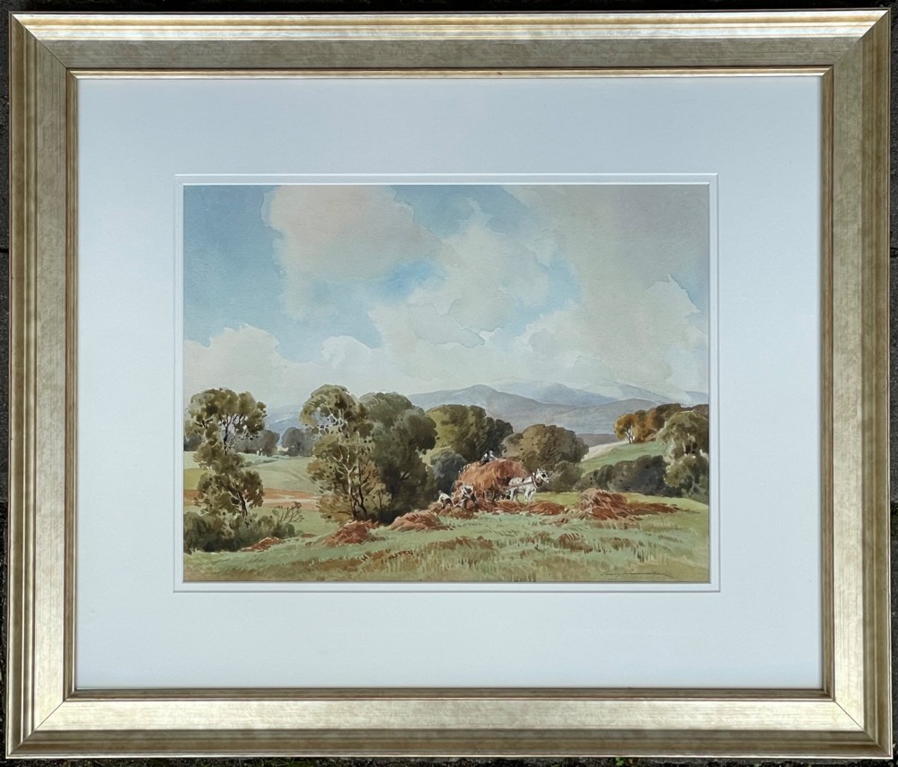 A framed watercolour painting depicting a rural harvest scene with figures, a horse-drawn cart, and rolling hills beneath a cloudy sky.