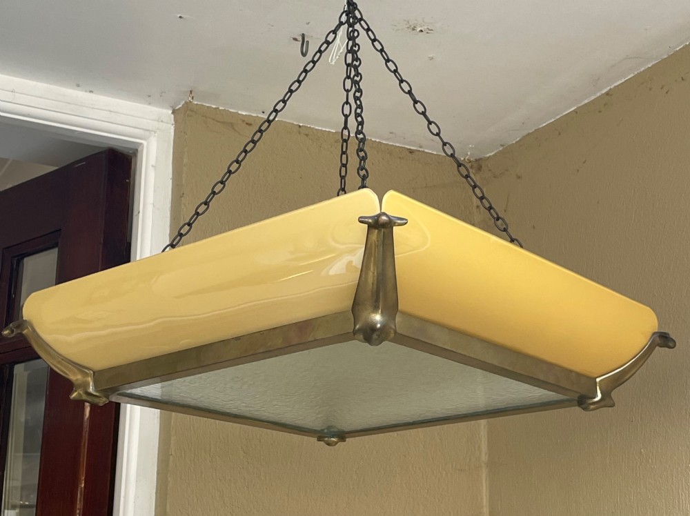 An Art Deco square pendant ceiling light featuring yellow glass side panels set within a brass frame, suspended by dark metal chains.