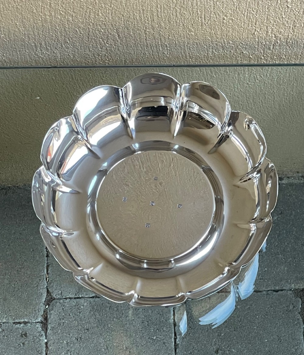A circular solid silver strawberry dish featuring fluted lobed edges and hallmarks stamped in the flat central well.