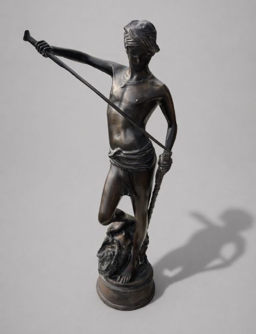fig 1. A dark patinated bronze statue of David sheathing his sword while standing with one foot on the severed head of Goliath.