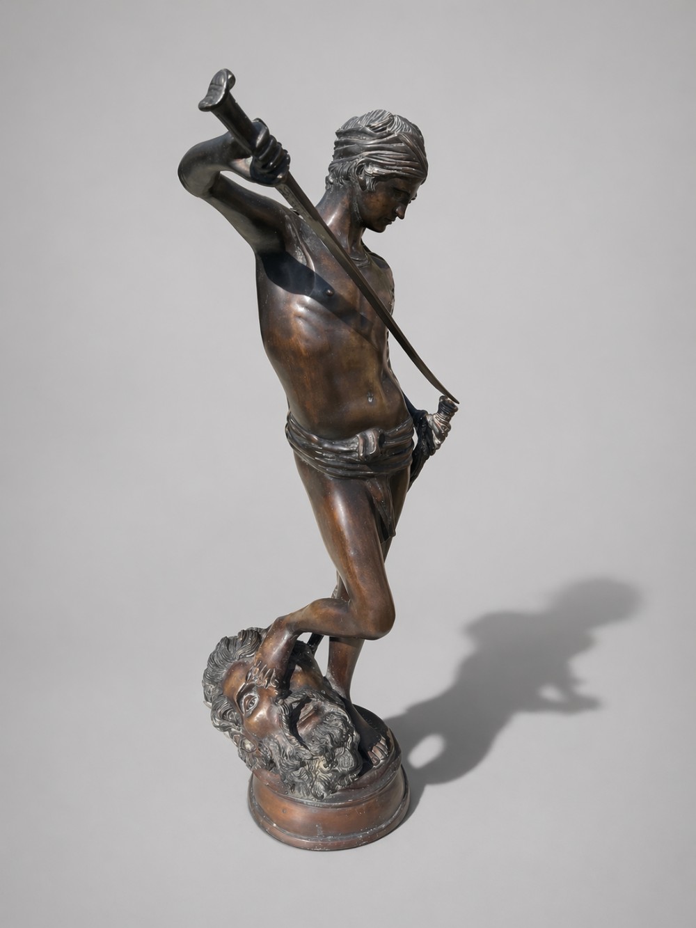 A dark patinated bronze statue of David sheathing his sword while standing with one foot on the severed head of Goliath.
