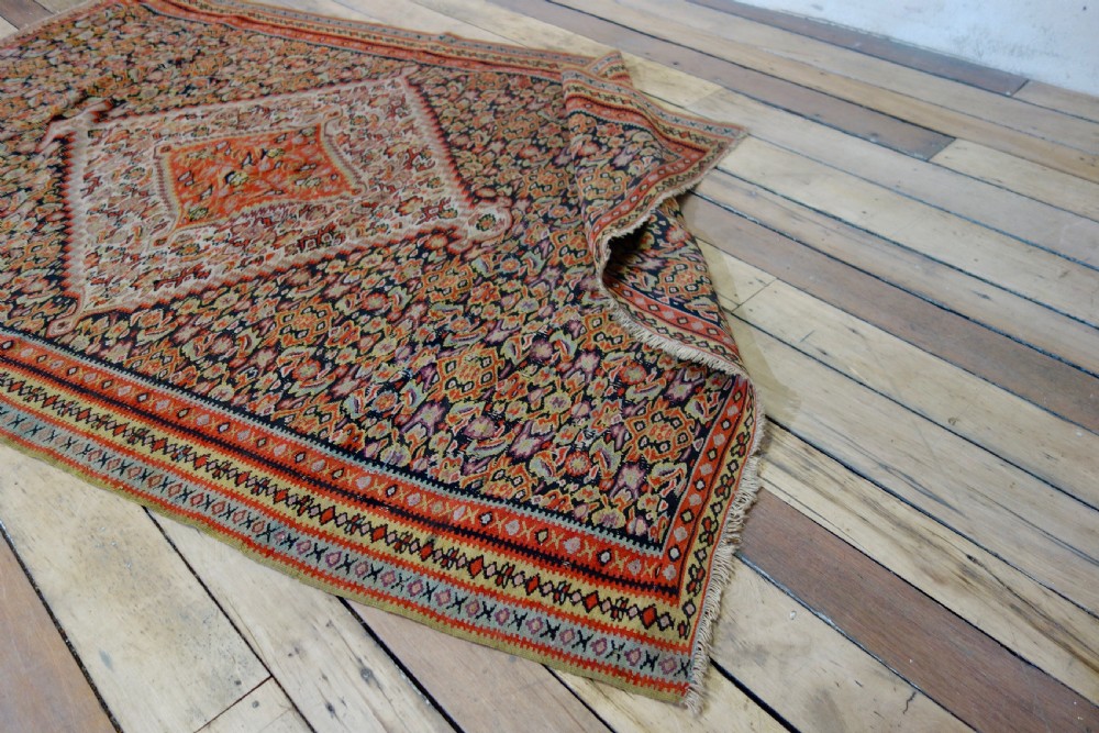 An antique hand-woven Senneh kilim rug featuring a prominent central diamond medallion surrounded by intricate repeating patterns in terracotta red, dark navy, and beige tones. View XI