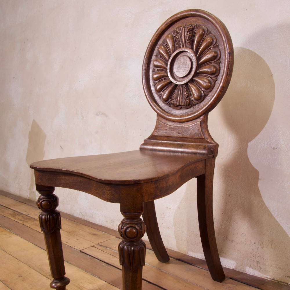 A 19th-century William IV hall chair made from elm and burr elm featuring a carved circular medallion back, solid wooden seat, turned front legs, and curved rear legs. View VII
