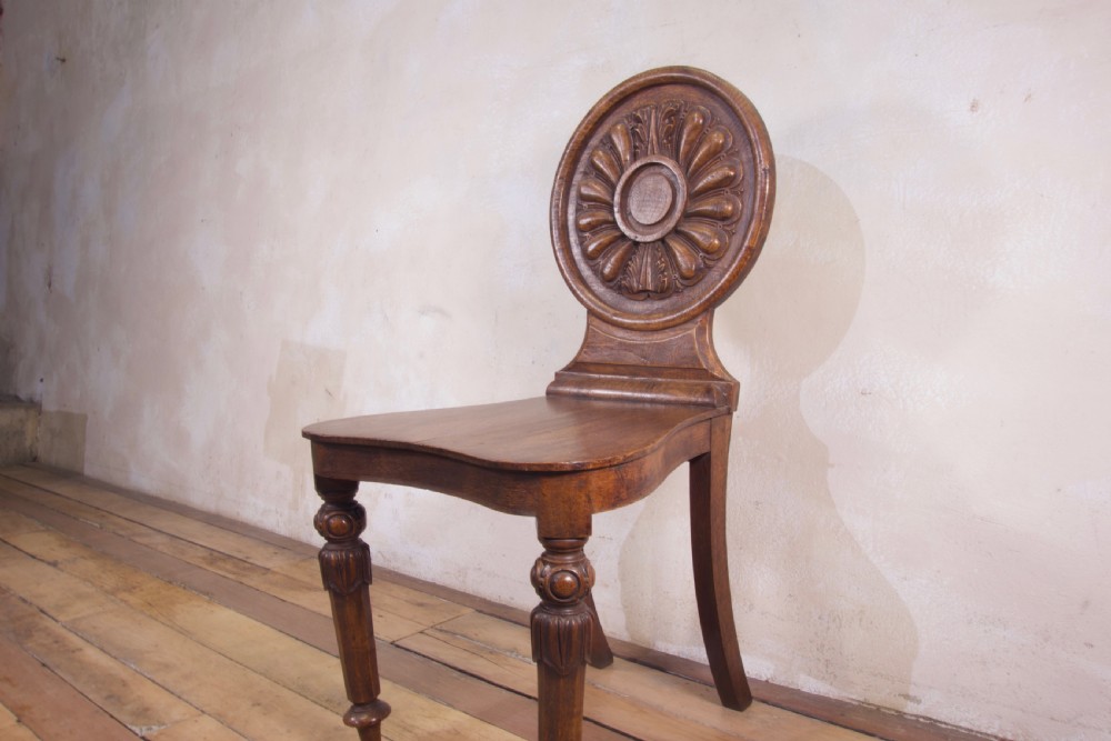 A 19th-century William IV hall chair made from elm and burr elm featuring a carved circular medallion back, solid wooden seat, turned front legs, and curved rear legs. View III