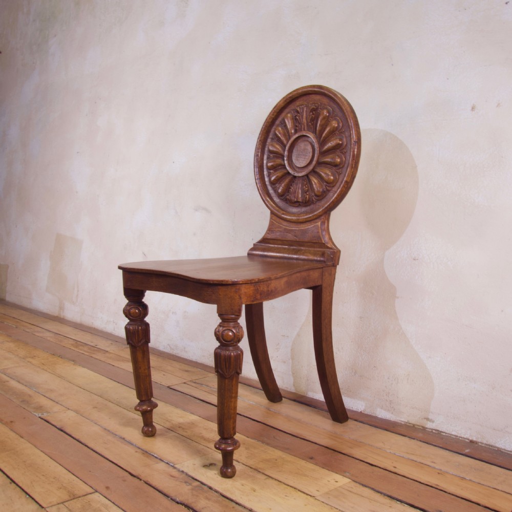 A 19th-century William IV hall chair made from elm and burr elm featuring a carved circular medallion back, solid wooden seat, turned front legs, and curved rear legs. View IV