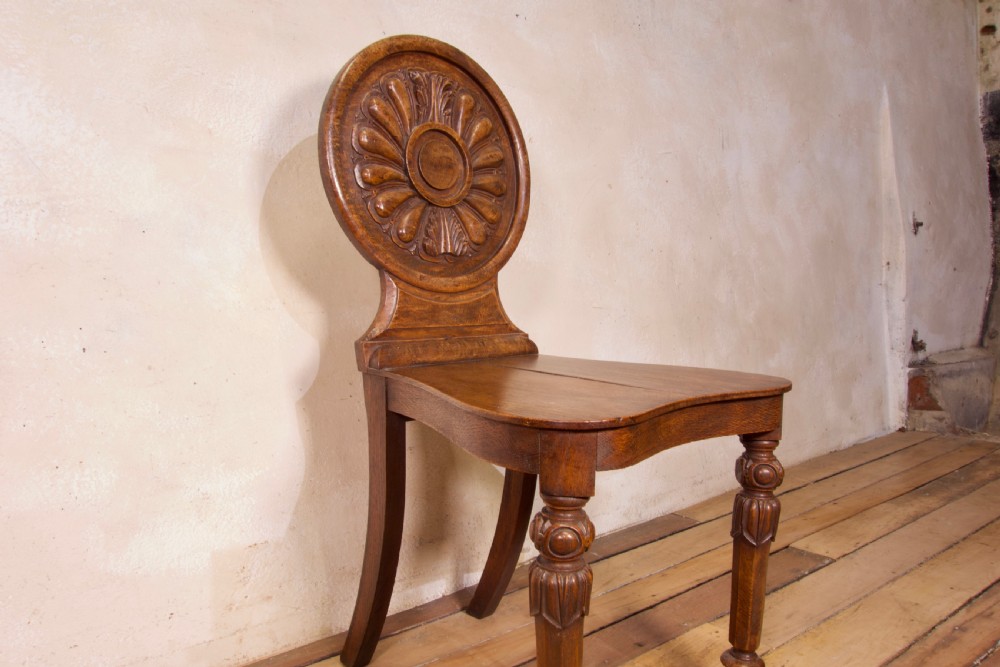 A 19th-century William IV hall chair made from elm and burr elm featuring a carved circular medallion back, solid wooden seat, turned front legs, and curved rear legs. View V