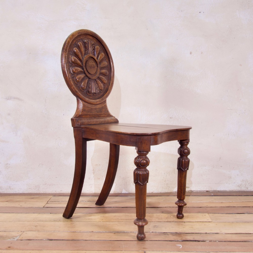 A 19th-century William IV hall chair made from elm and burr elm featuring a carved circular medallion back, solid wooden seat, turned front legs, and curved rear legs.
