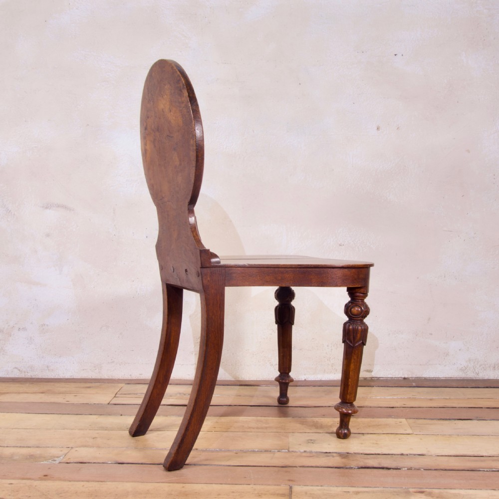 A 19th-century William IV hall chair made from elm and burr elm featuring a carved circular medallion back, solid wooden seat, turned front legs, and curved rear legs. View VIII