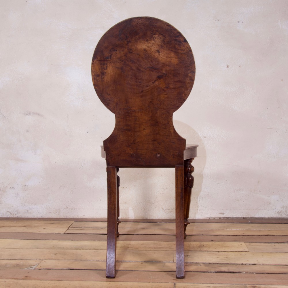 A 19th-century William IV hall chair made from elm and burr elm featuring a carved circular medallion back, solid wooden seat, turned front legs, and curved rear legs. View IX