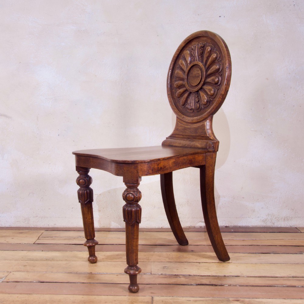 A 19th-century William IV hall chair made from elm and burr elm featuring a carved circular medallion back, solid wooden seat, turned front legs, and curved rear legs. View XI