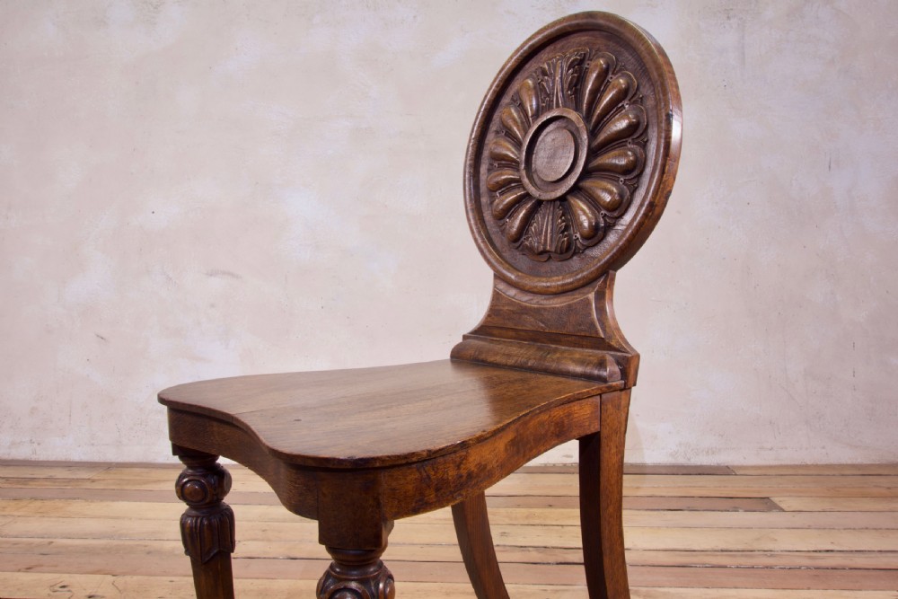 A 19th-century William IV hall chair made from elm and burr elm featuring a carved circular medallion back, solid wooden seat, turned front legs, and curved rear legs. View XII