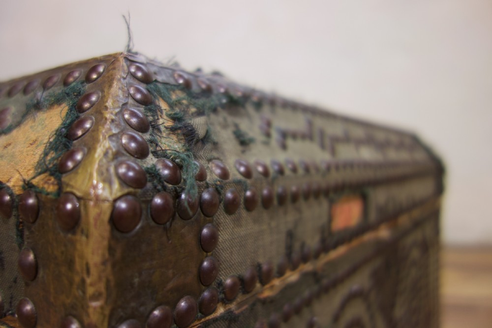 A small 19th-century French trunk featuring olive green fabric, brass stud patterning, iron side handles, and wooden bun feet. View XIV