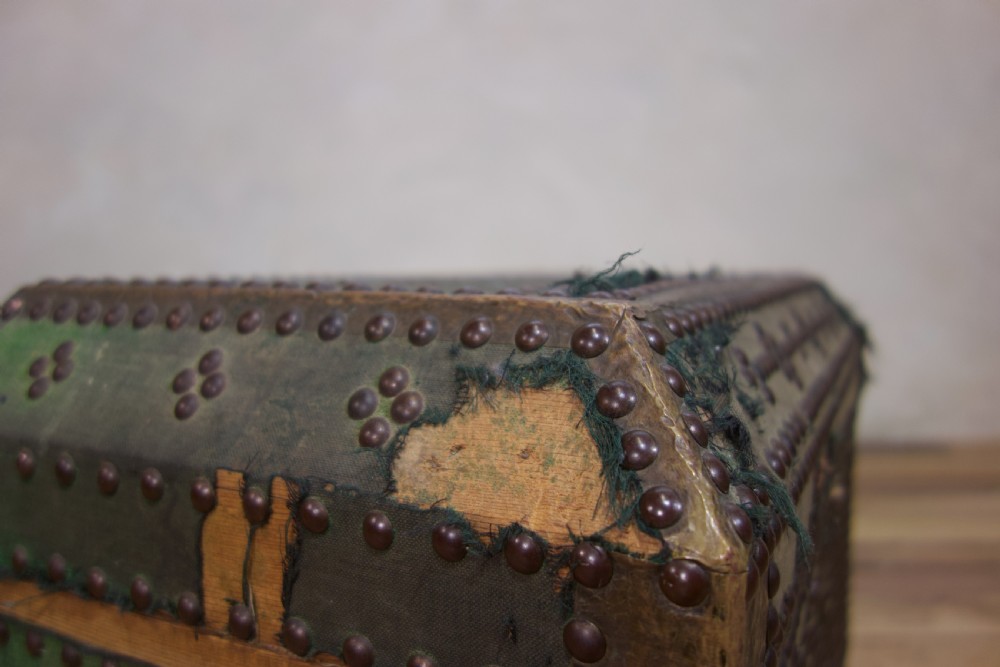 A small 19th-century French trunk featuring olive green fabric, brass stud patterning, iron side handles, and wooden bun feet. View III