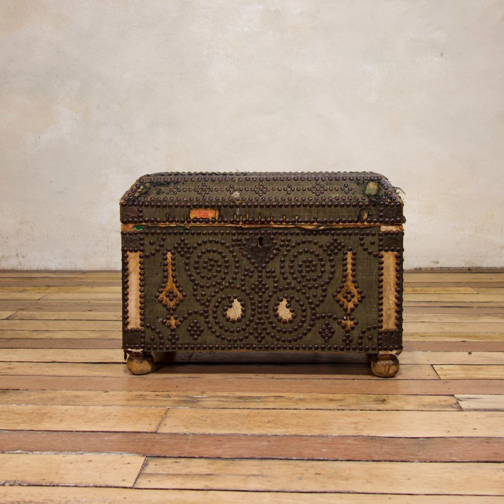 A small 19th-century French trunk featuring olive green fabric, brass stud patterning, iron side handles, and wooden bun feet. View IV