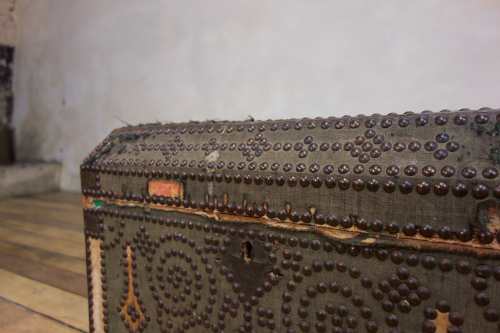A small 19th-century French trunk featuring olive green fabric, brass stud patterning, iron side handles, and wooden bun feet. View VII