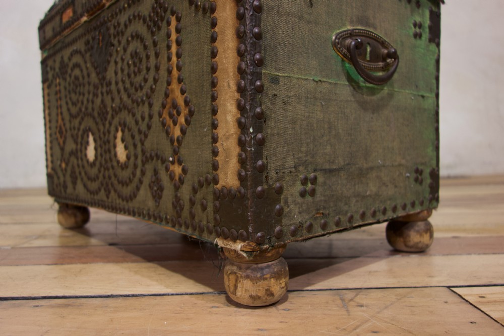 A small 19th-century French trunk featuring olive green fabric, brass stud patterning, iron side handles, and wooden bun feet. View VIII
