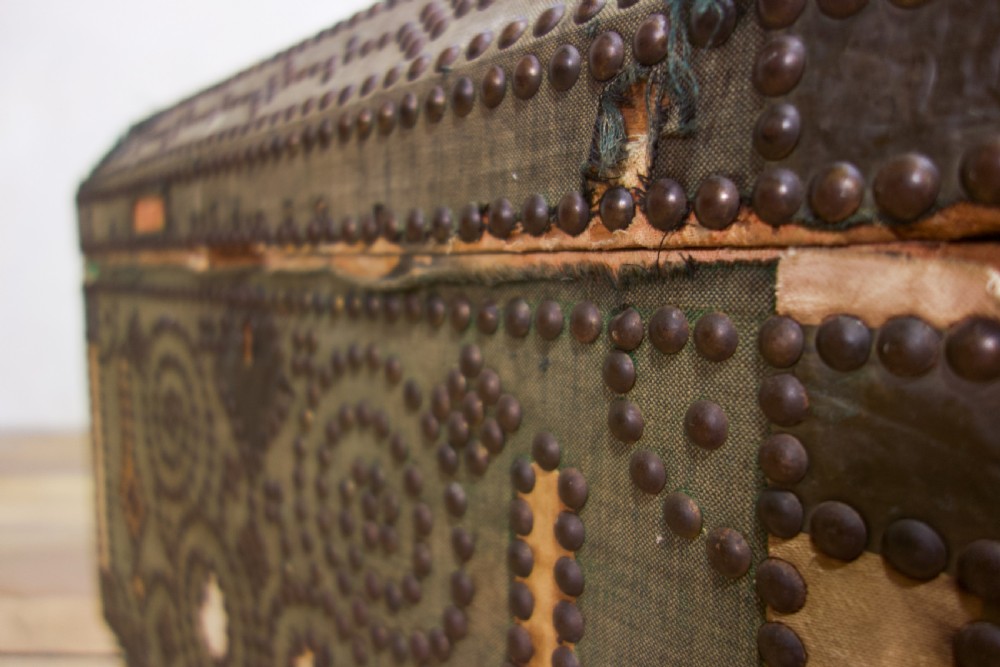 A small 19th-century French trunk featuring olive green fabric, brass stud patterning, iron side handles, and wooden bun feet. View IX