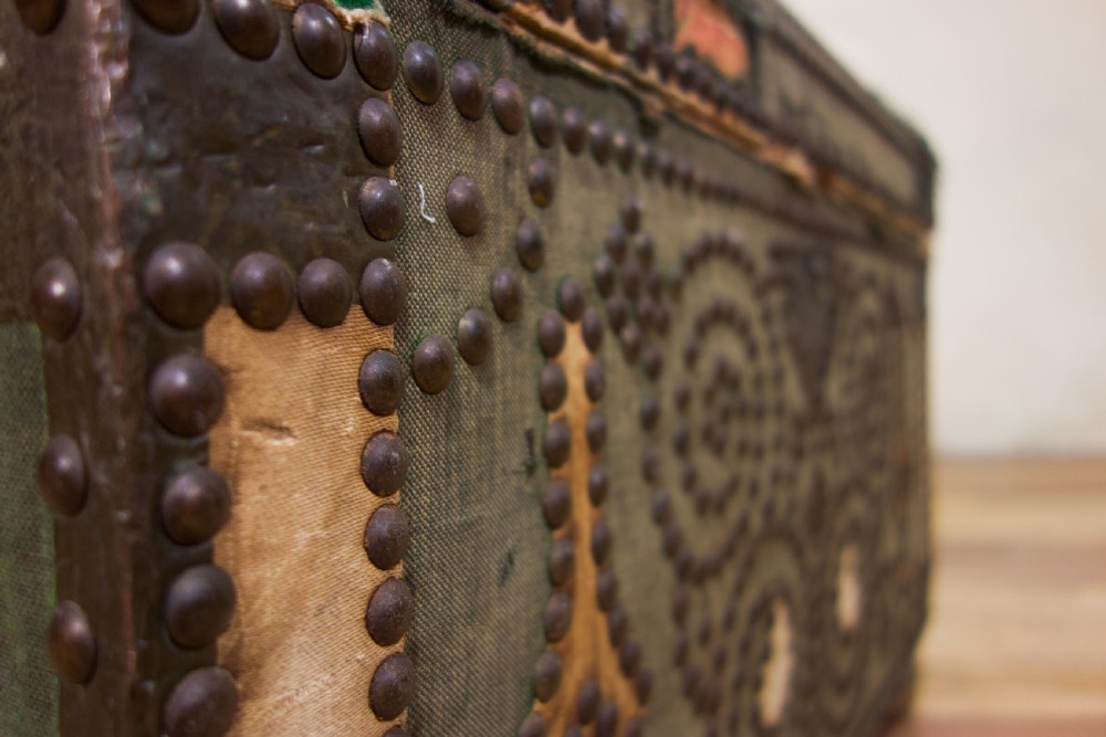 A small 19th-century French trunk featuring olive green fabric, brass stud patterning, iron side handles, and wooden bun feet. View XII