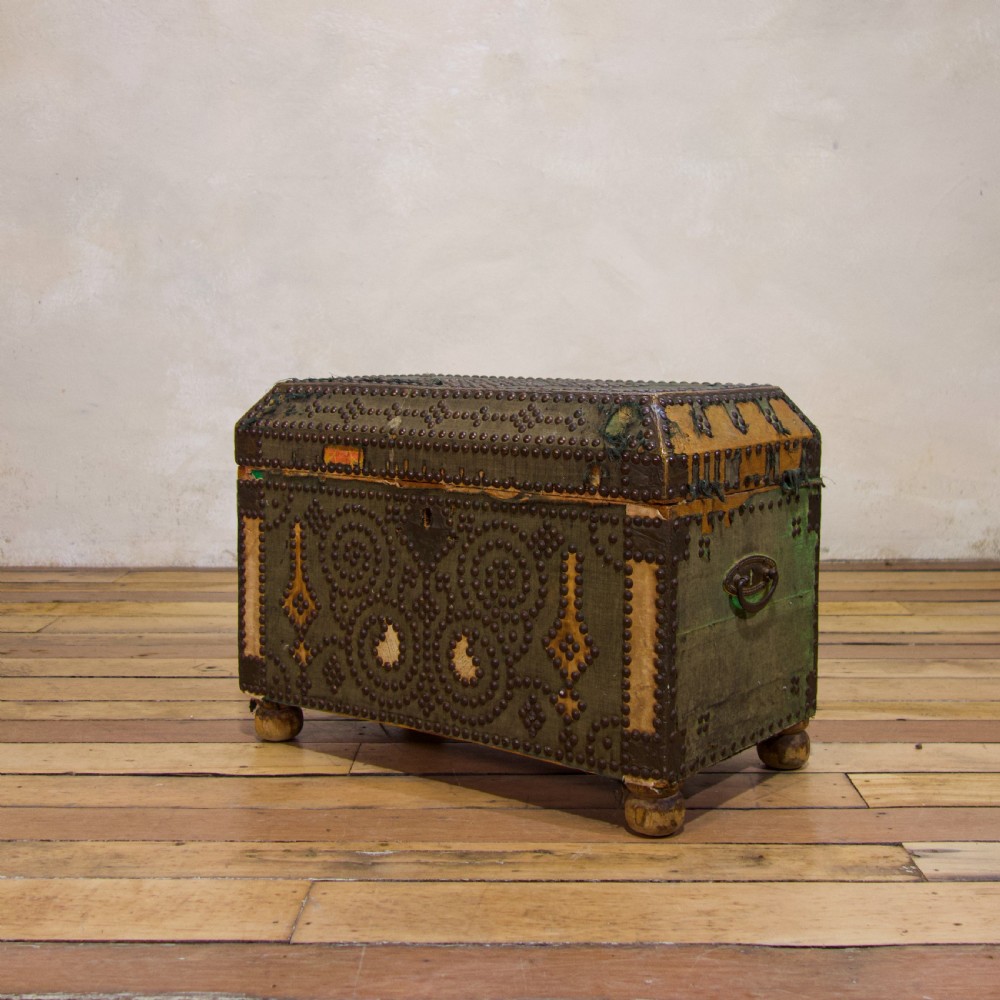 A small 19th-century French trunk featuring olive green fabric, brass stud patterning, iron side handles, and wooden bun feet.