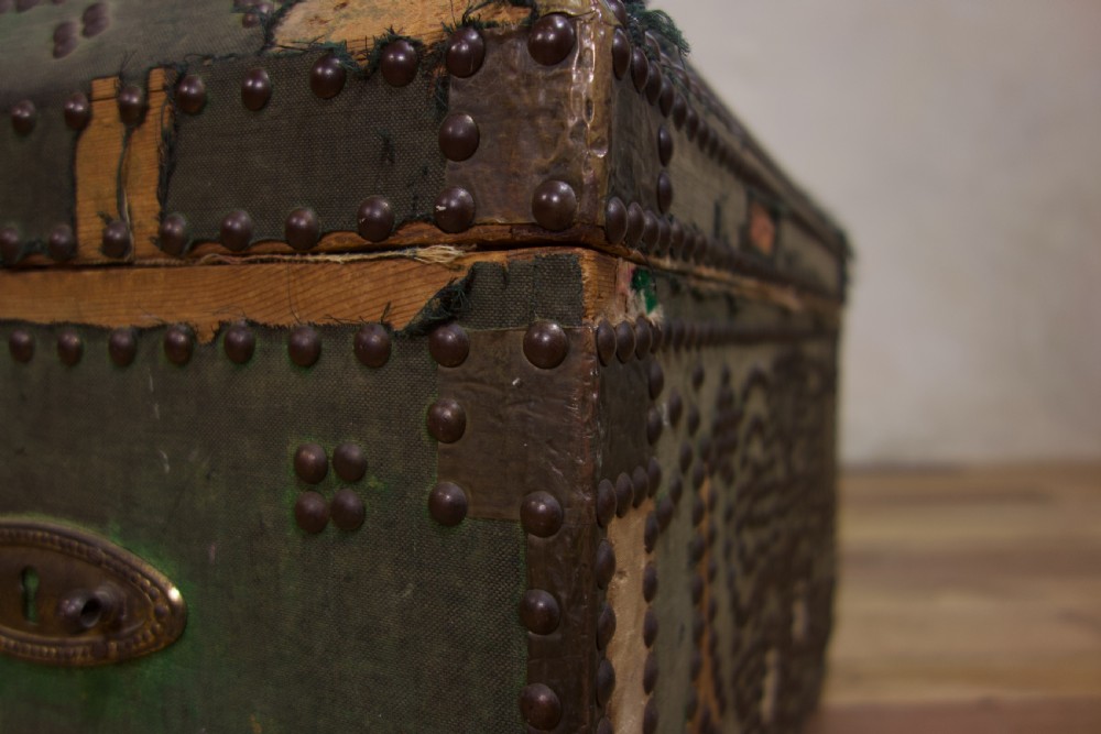 A small 19th-century French trunk featuring olive green fabric, brass stud patterning, iron side handles, and wooden bun feet. View XV
