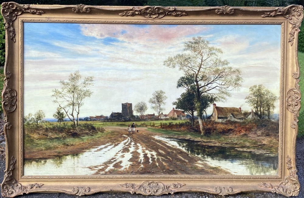 A large 19th-century oil painting depicting a muddy country lane leading past thatched cottages towards a village church, housed in an ornate gilt frame.