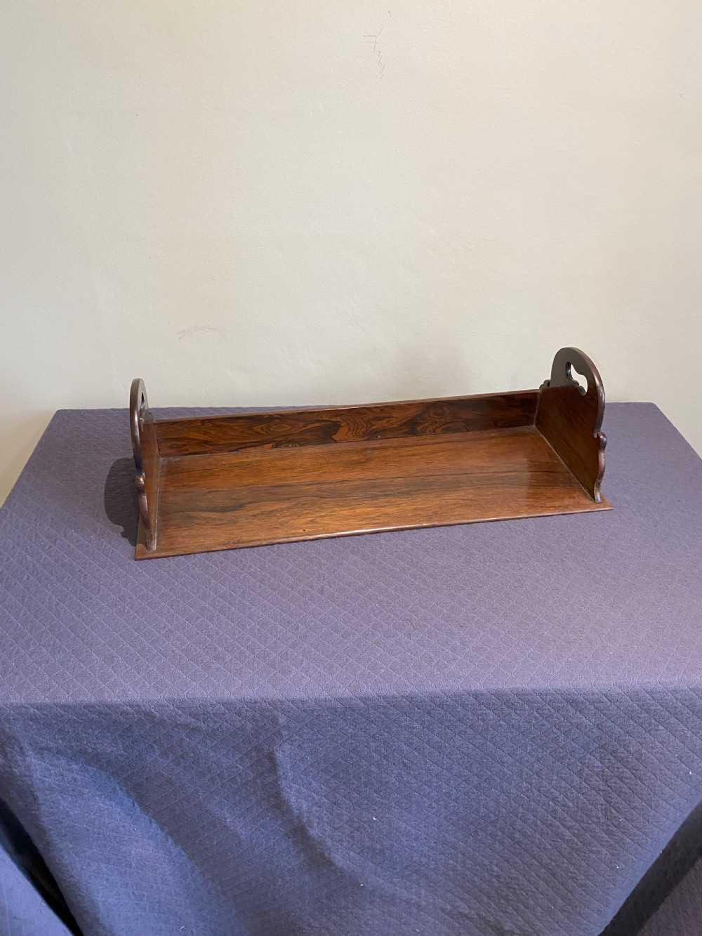 A mid-19th-century dark rosewood tabletop book rack featuring open cut-out side handles and a flat rectangular base.