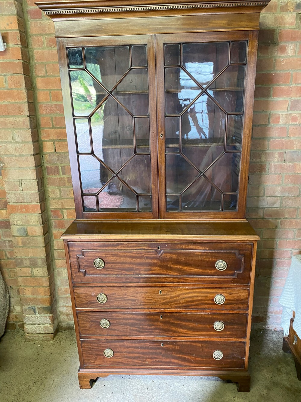 A George III mahogany secretaire bookcase featuring an upper glazed cabinet with geometric astragal bars, positioned above a lower chest of drawers with round brass handles on bracket feet.