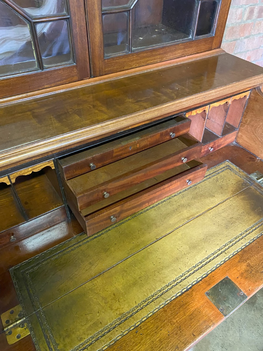 A George III mahogany secretaire bookcase featuring an upper glazed cabinet with geometric astragal bars, positioned above a lower chest of drawers with round brass handles on bracket feet. View II