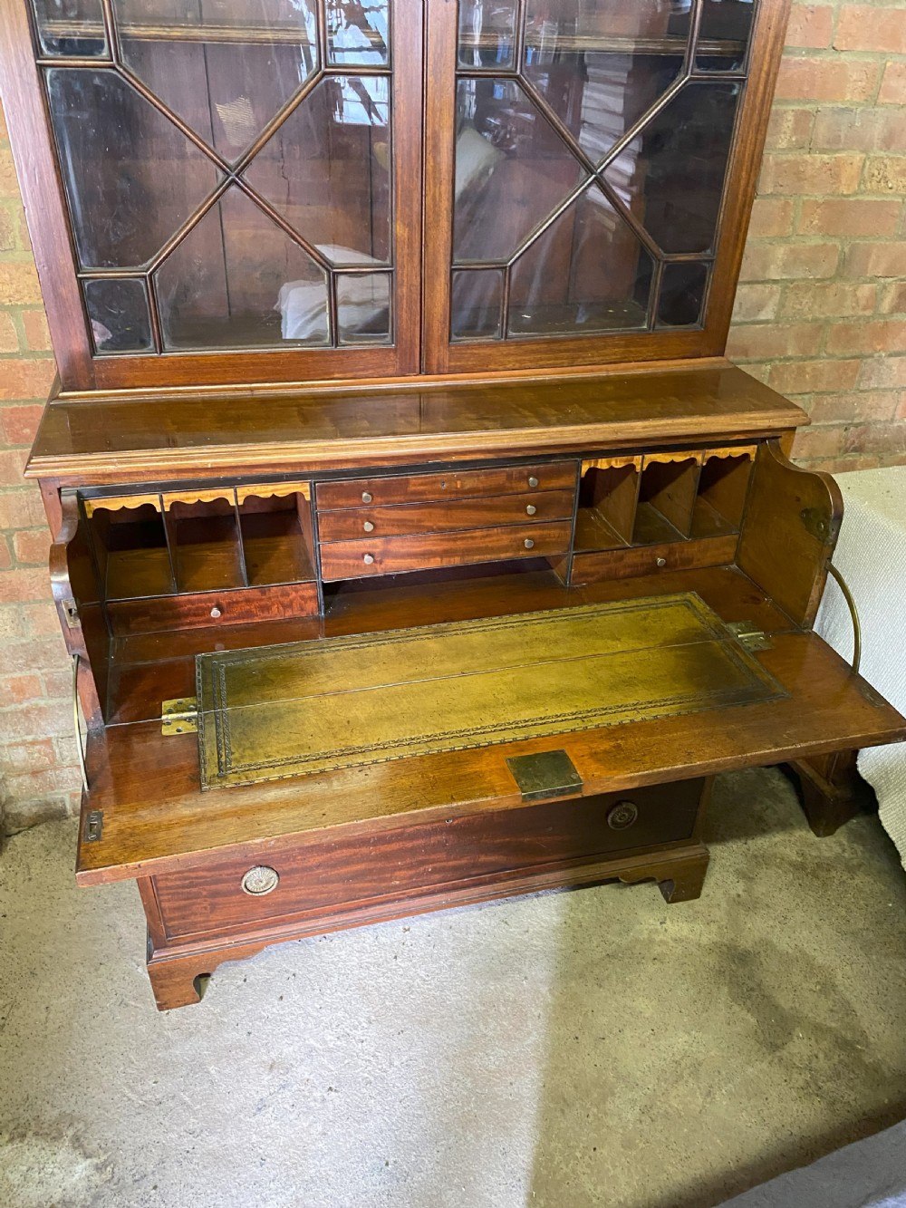 A George III mahogany secretaire bookcase featuring an upper glazed cabinet with geometric astragal bars, positioned above a lower chest of drawers with round brass handles on bracket feet. View III
