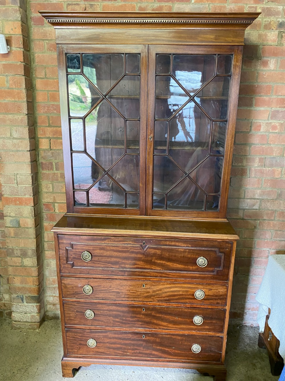 A George III mahogany secretaire bookcase featuring an upper glazed cabinet with geometric astragal bars, positioned above a lower chest of drawers with round brass handles on bracket feet. View VII