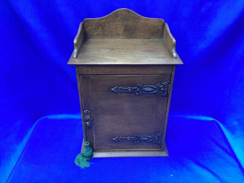 fig 1. An Arts and Crafts medium brown oak key cabinet featuring an arched shaped gallery top and elaborate metal strap hinges on the single cupboard door.