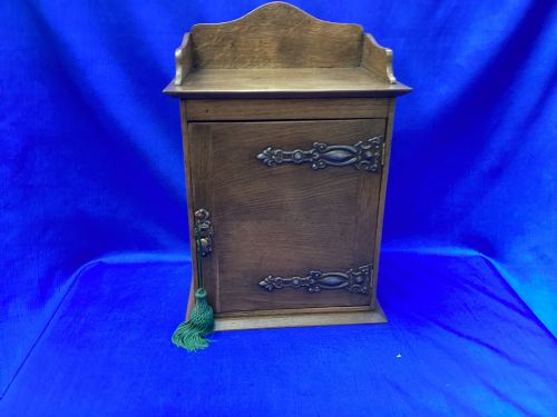 fig 2. An Arts and Crafts medium brown oak key cabinet featuring an arched shaped gallery top and elaborate metal strap hinges on the single cupboard door.