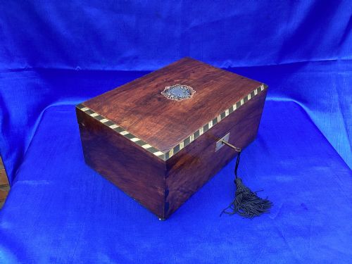 fig 1. A rectangular Victorian mahogany box featuring decorative geometric inlay borders, a central crest motif on the lid, and a brass keyhole with a key and black tassel.