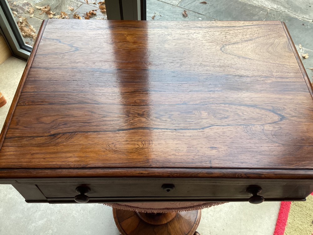 A 19th-century rosewood sewing table featuring a top drawer, a pink pleated silk work basket supported by a U-shaped frame, and a pedestal base with carved scroll feet. View II
