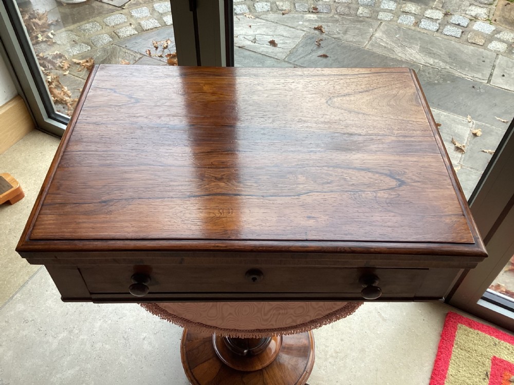A 19th-century rosewood sewing table featuring a top drawer, a pink pleated silk work basket supported by a U-shaped frame, and a pedestal base with carved scroll feet. View IV