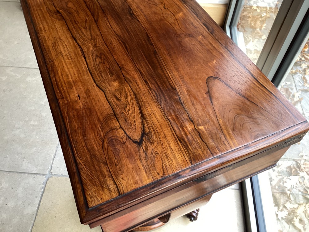 A 19th-century rosewood sewing table featuring a top drawer, a pink pleated silk work basket supported by a U-shaped frame, and a pedestal base with carved scroll feet. View V