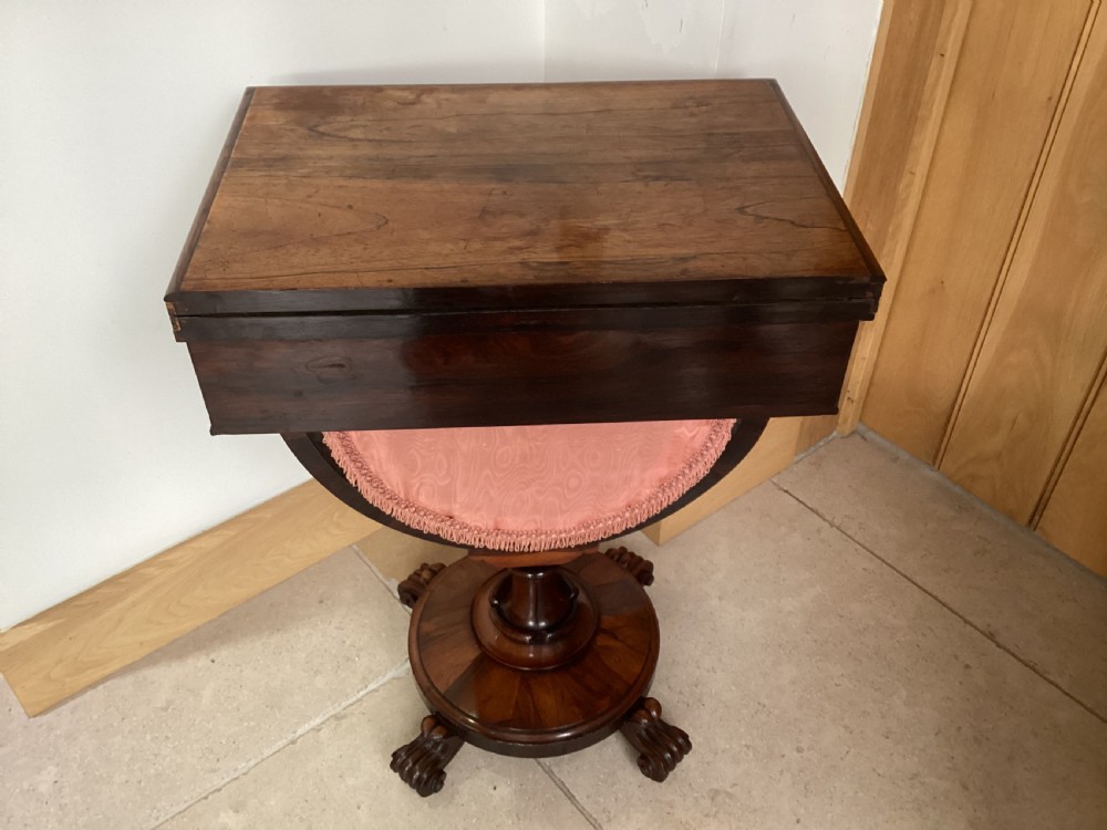 A 19th-century rosewood sewing table featuring a top drawer, a pink pleated silk work basket supported by a U-shaped frame, and a pedestal base with carved scroll feet. View VI