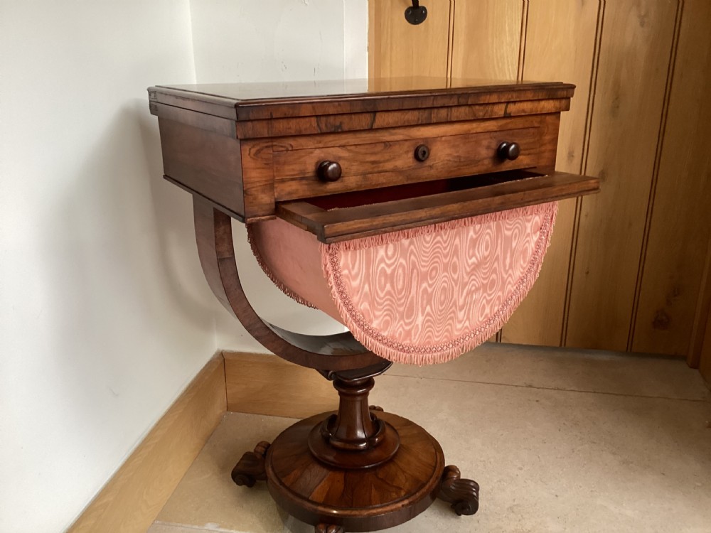 A 19th-century rosewood sewing table featuring a top drawer, a pink pleated silk work basket supported by a U-shaped frame, and a pedestal base with carved scroll feet. View VII