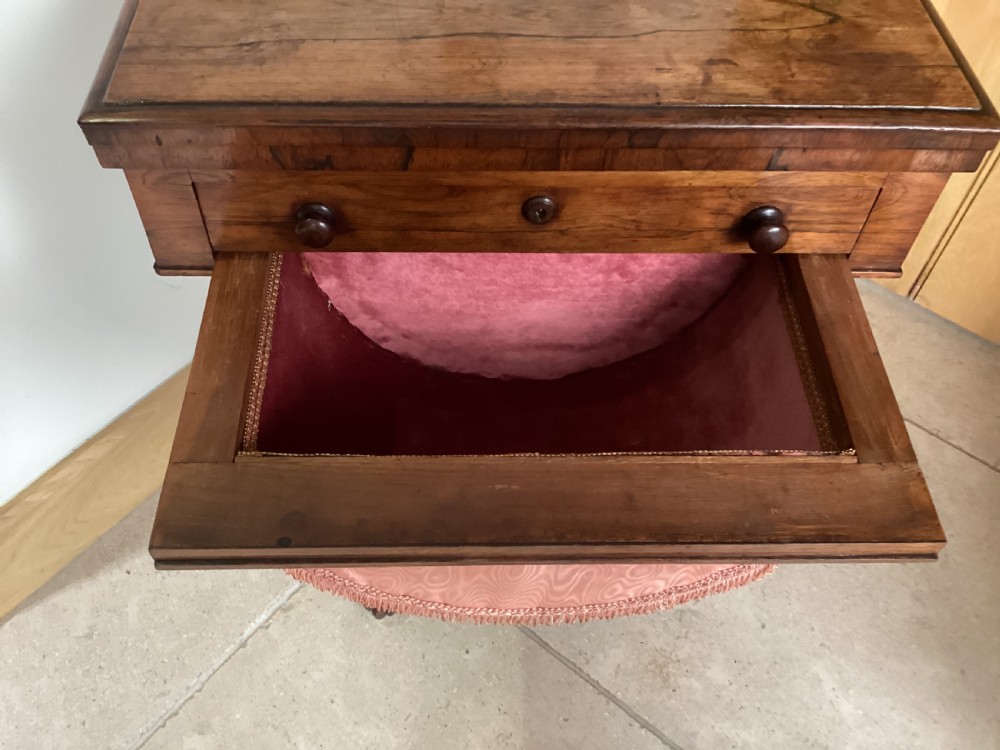 A 19th-century rosewood sewing table featuring a top drawer, a pink pleated silk work basket supported by a U-shaped frame, and a pedestal base with carved scroll feet. View VIII