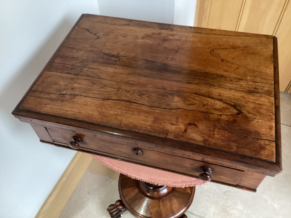 A 19th-century rosewood sewing table featuring a top drawer, a pink pleated silk work basket supported by a U-shaped frame, and a pedestal base with carved scroll feet. View IX