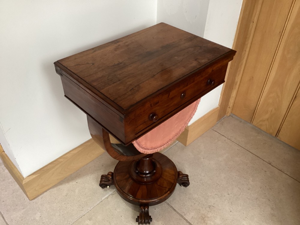 A 19th-century rosewood sewing table featuring a top drawer, a pink pleated silk work basket supported by a U-shaped frame, and a pedestal base with carved scroll feet. View XIV