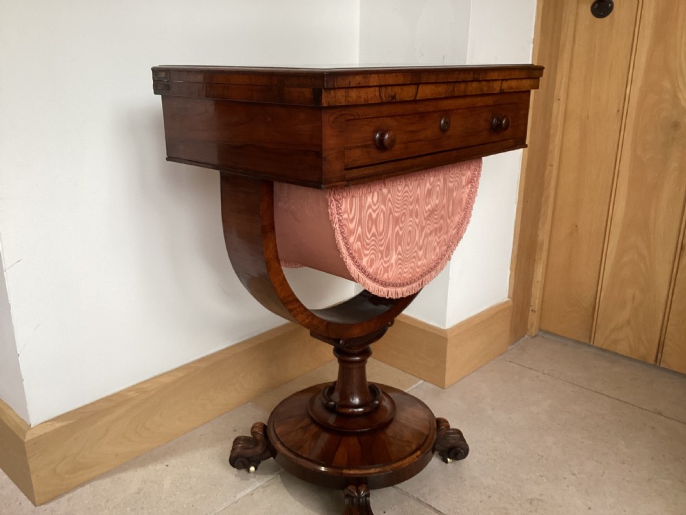 A 19th-century rosewood sewing table featuring a top drawer, a pink pleated silk work basket supported by a U-shaped frame, and a pedestal base with carved scroll feet. View XV
