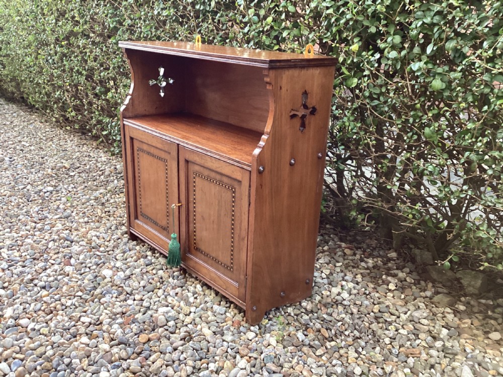 An Arts and Crafts mahogany wall cupboard featuring an open upper shelf, two inlaid lower doors, brass mounting brackets, and a key with a green tassel. View XIV
