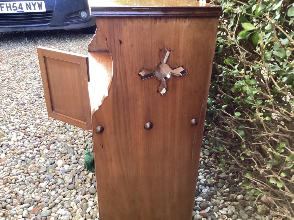 An Arts and Crafts mahogany wall cupboard featuring an open upper shelf, two inlaid lower doors, brass mounting brackets, and a key with a green tassel. View XV