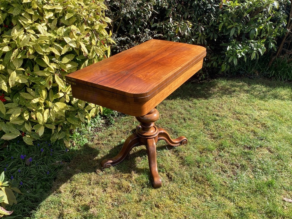 Victorian rosewood fold-over games table supported by a central turned pedestal column and four carved scroll feet. View II