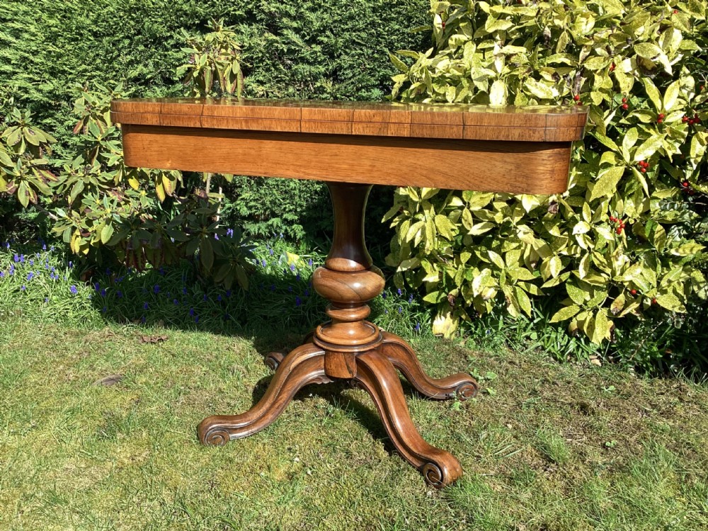 Victorian rosewood fold-over games table supported by a central turned pedestal column and four carved scroll feet. View IV
