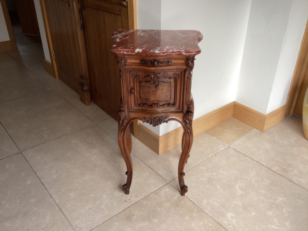 An antique French Rococo style carved walnut pot cupboard with a contoured red marble top and slender cabriole legs.
