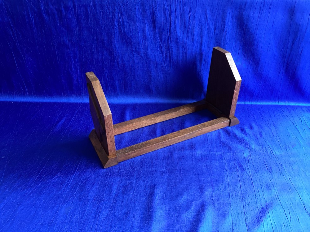 A solid oak Art Deco desktop book trough featuring angled side supports with carved horse silhouettes connected by twin horizontal rails.