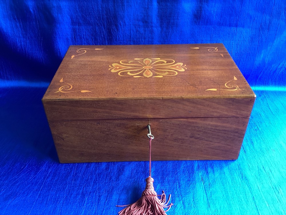 A rectangular dark walnut wooden writing slope featuring stylised floral marquetry inlay across the top lid and a key with a pink tassel in the front lock.